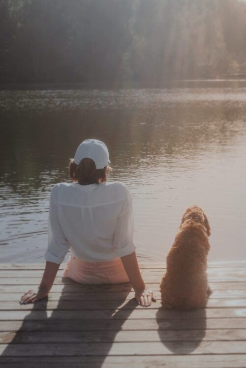 Eine Frau und ihr Hund sitzen auf dem Steg und schauen auf einen See